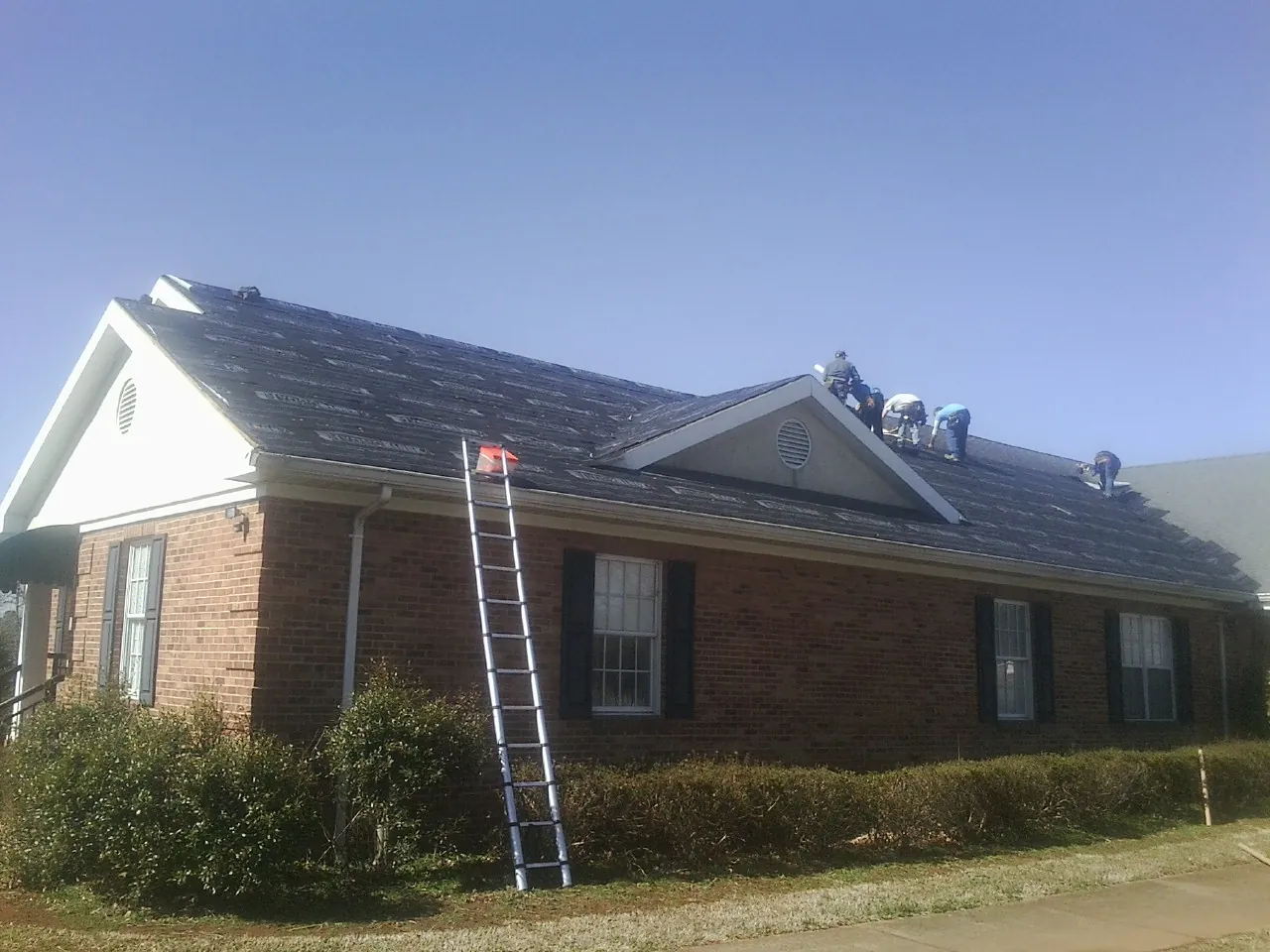 Crew tearing shingles off a brick ranch roof with a ladder set — Metal Roof Repair work by our crew in Brewer