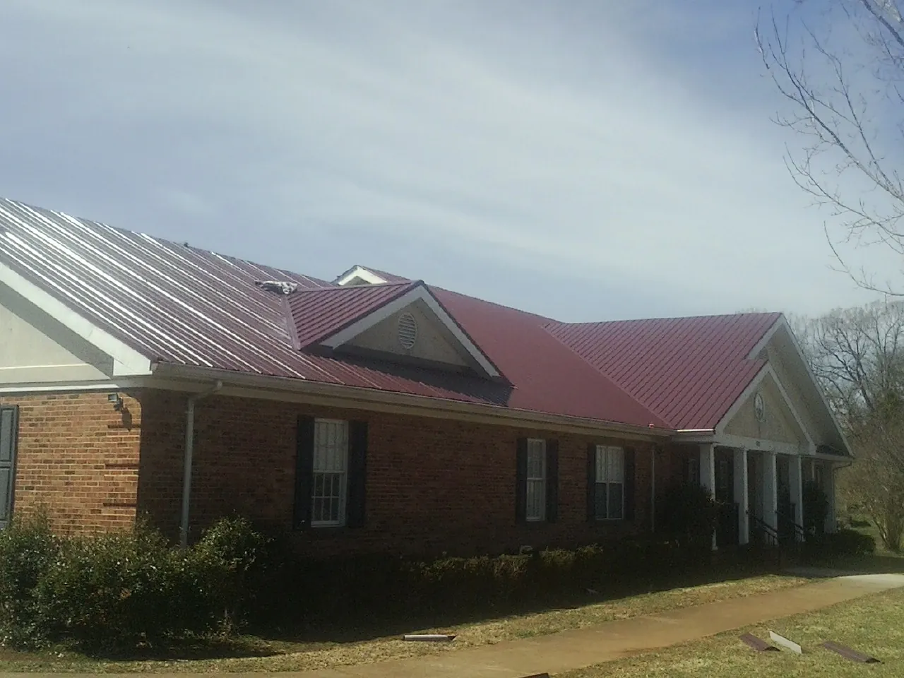 Red metal roof with gabled entries on a long brick building, from a Hail Damage Roof Repair job in Brewer