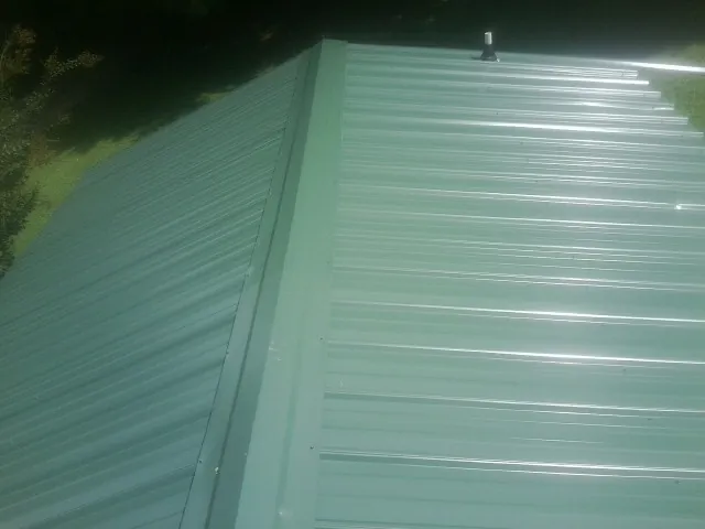 New green metal panels meeting at the ridge of a roof — Flat Roof Repair work by our crew in Brewer