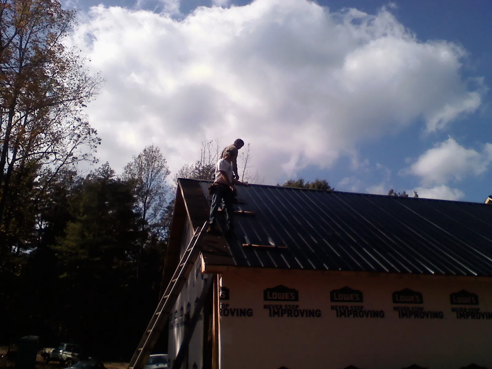 Roofer fastening dark metal panels high against a cloudy sky, from a Roof Inspection job in Brewer